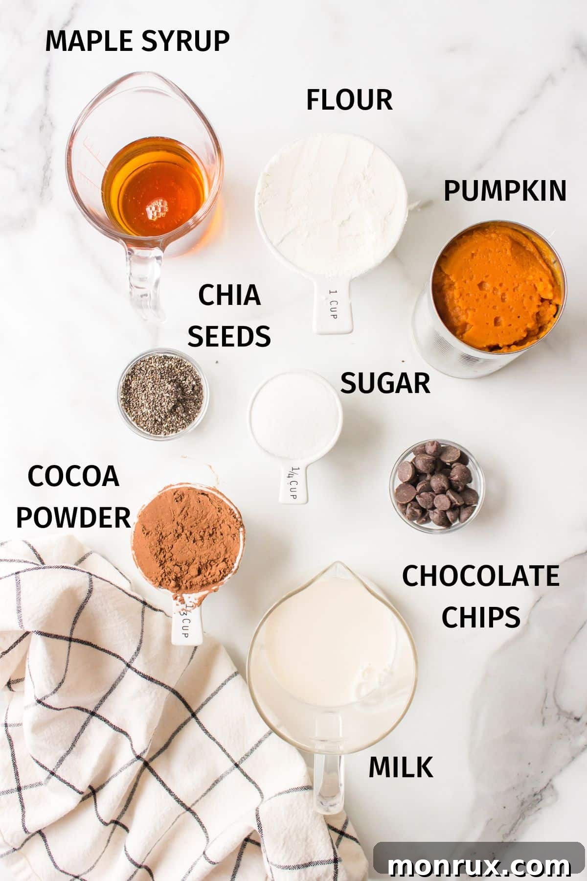 Various ingredients for vegan pumpkin brownies, including pumpkin puree, flour, cocoa powder, and maple syrup, neatly arranged in small bowls on a white countertop.