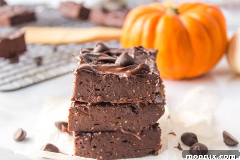 Three perfectly stacked vegan pumpkin brownies on a white counter, highlighting their inviting texture.