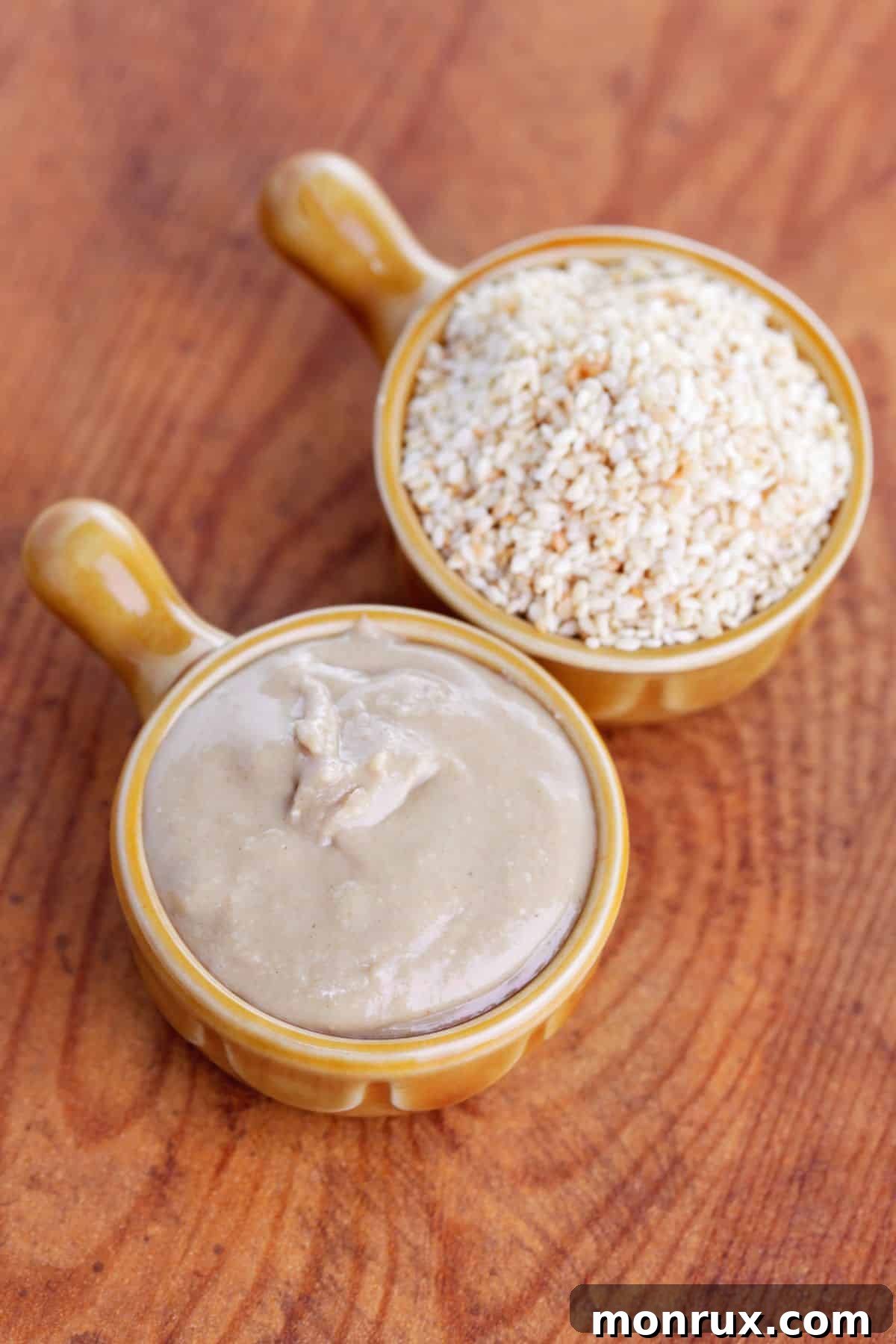 Bowls of sesame seeds and tahini on wooden surface.
