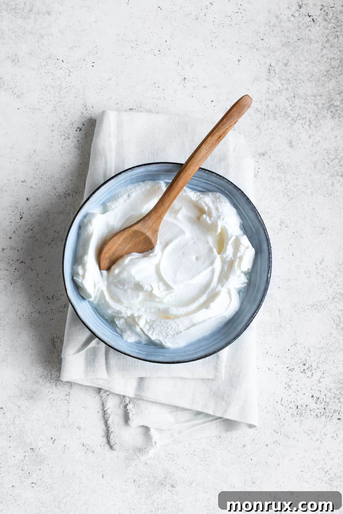 Bowl of greek yogurt with spoon on light surface.