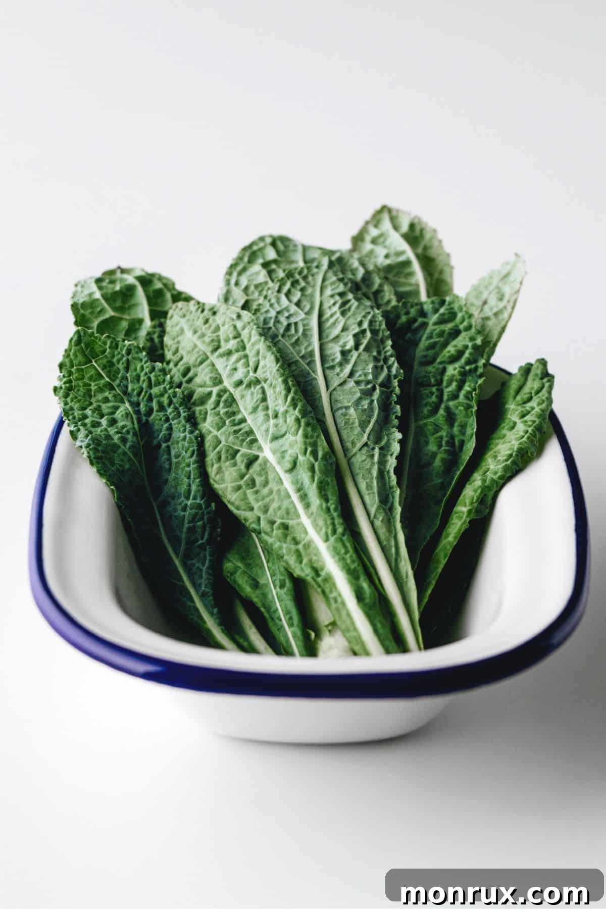 Bowl of kale leaves on white surface.