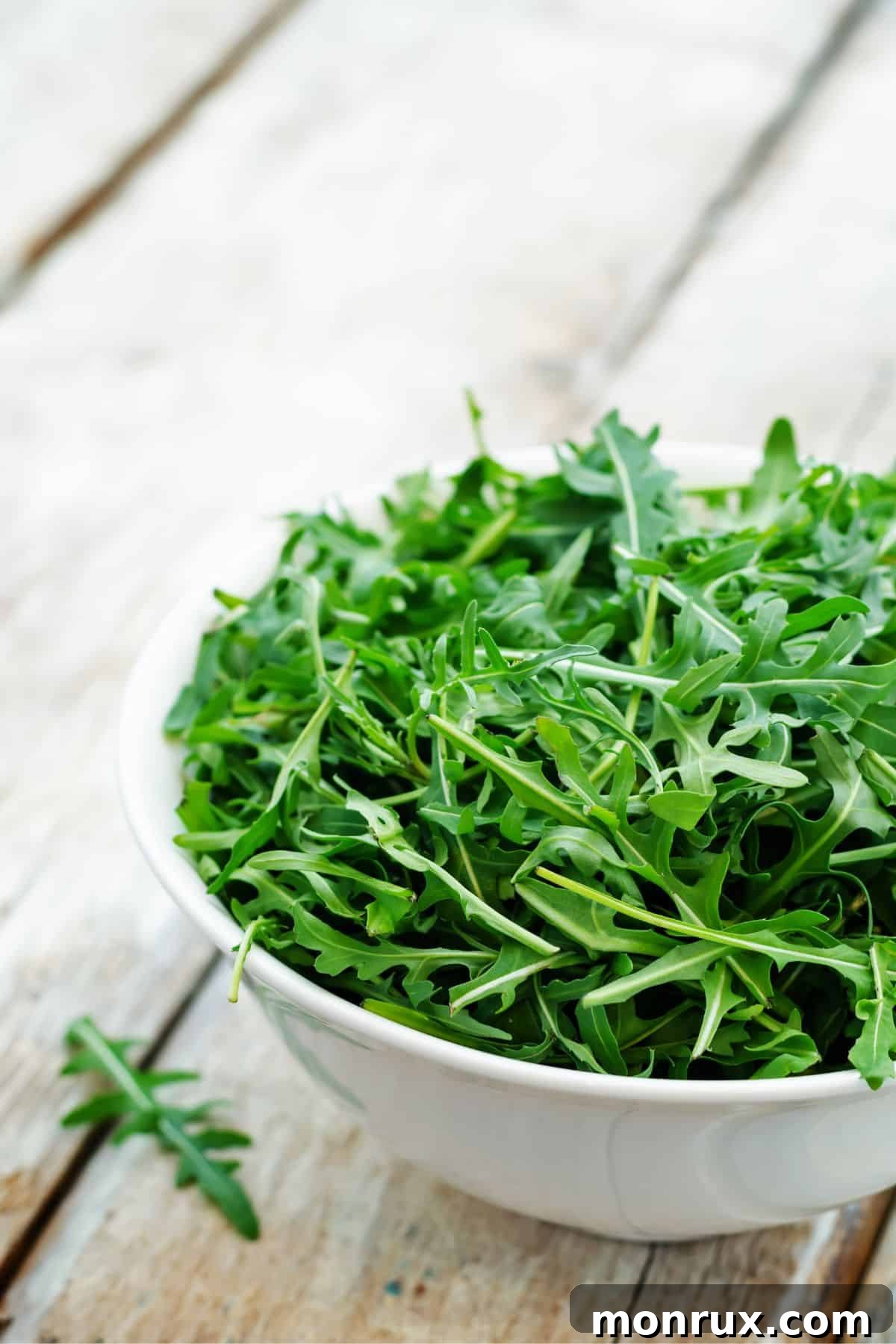 Bowl of arugula on wooden surface.