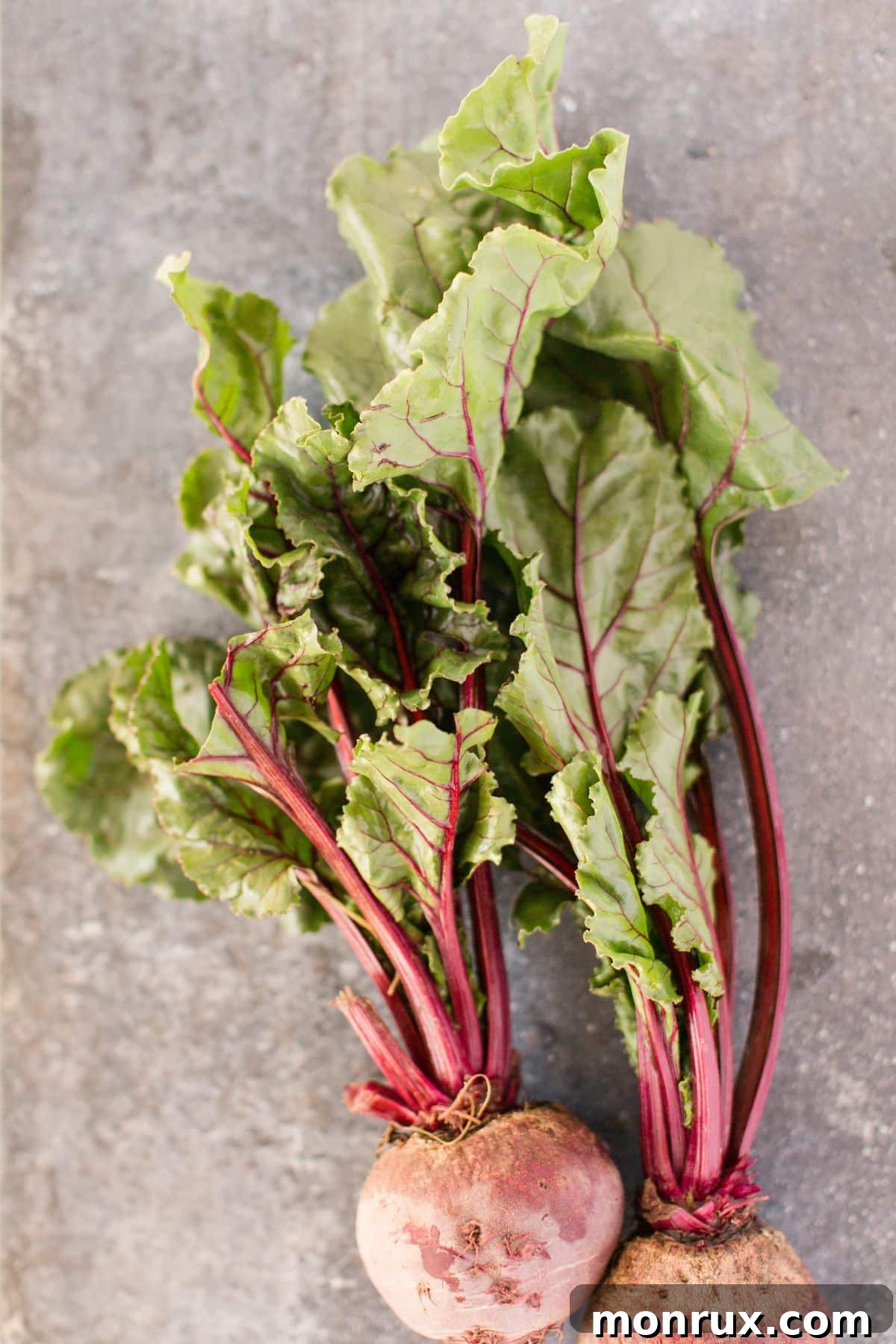 Beet greens with beets attached on dark surface.