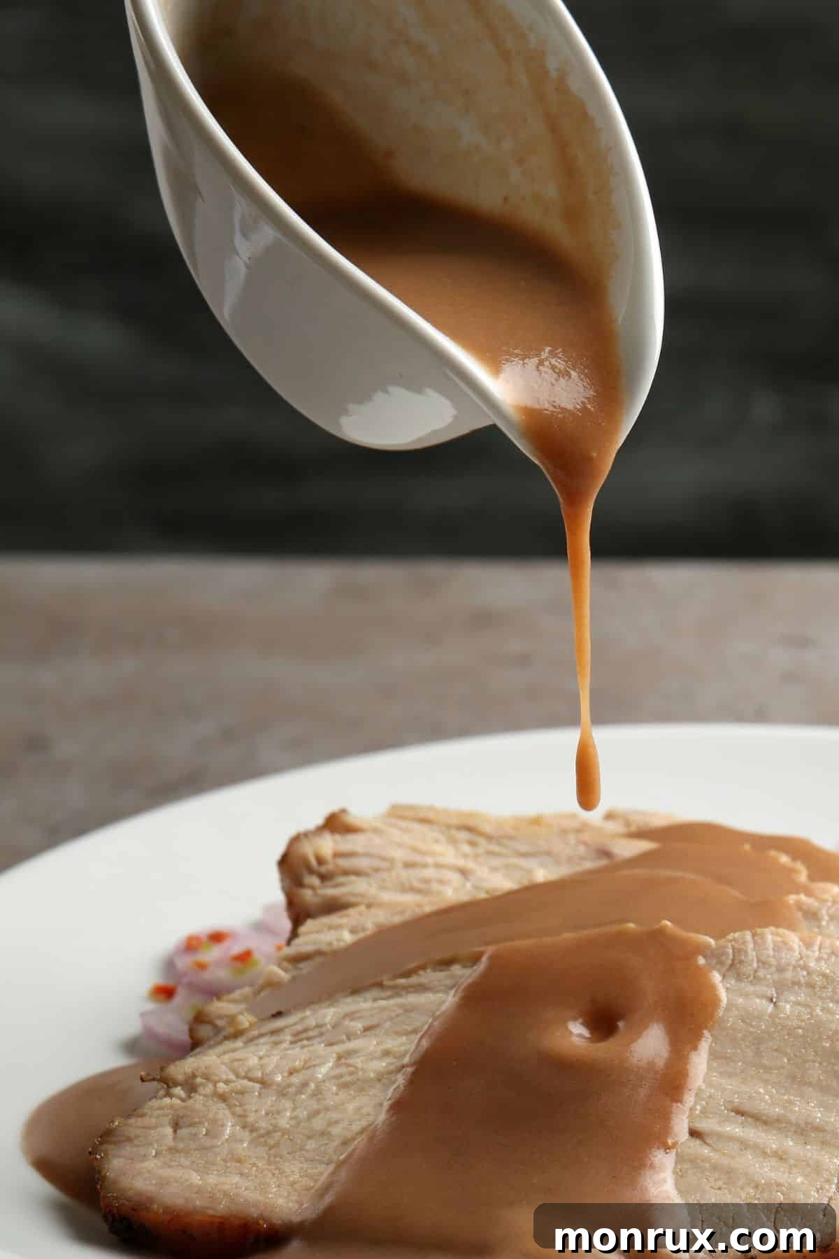 A hand pouring rich dairy-free gravy from a gravy boat over tender slices of roasted turkey on a white plate, ready for a festive meal.