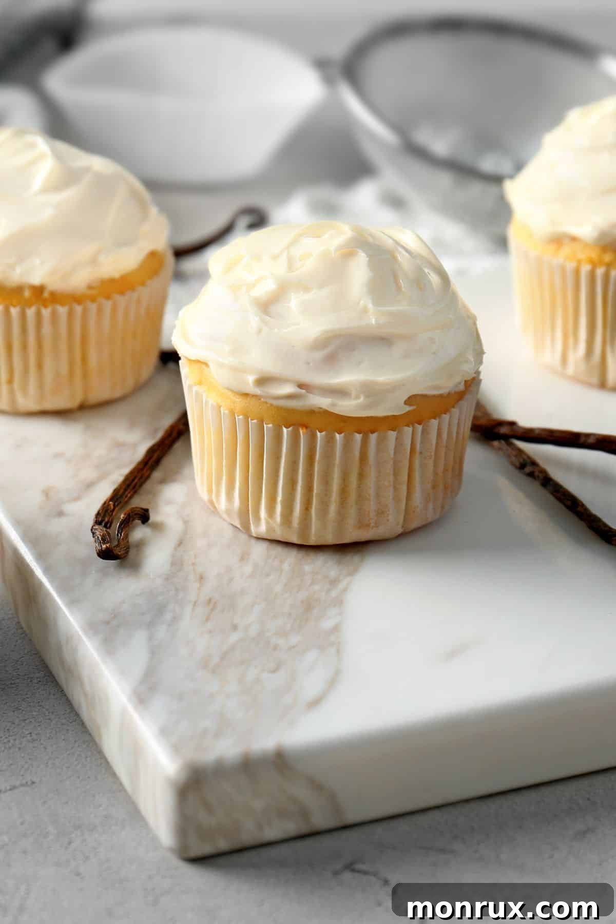 Two vanilla gluten-free and dairy-free cupcakes perfectly frosted on a pristine white marble surface.