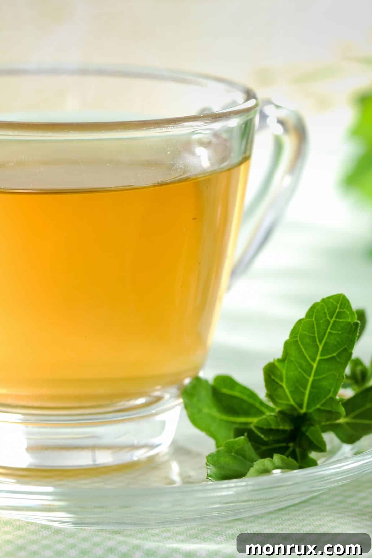 A transparent glass cup filled with steaming green tea, placed on a light wooden surface, signifying health and natural detoxification.