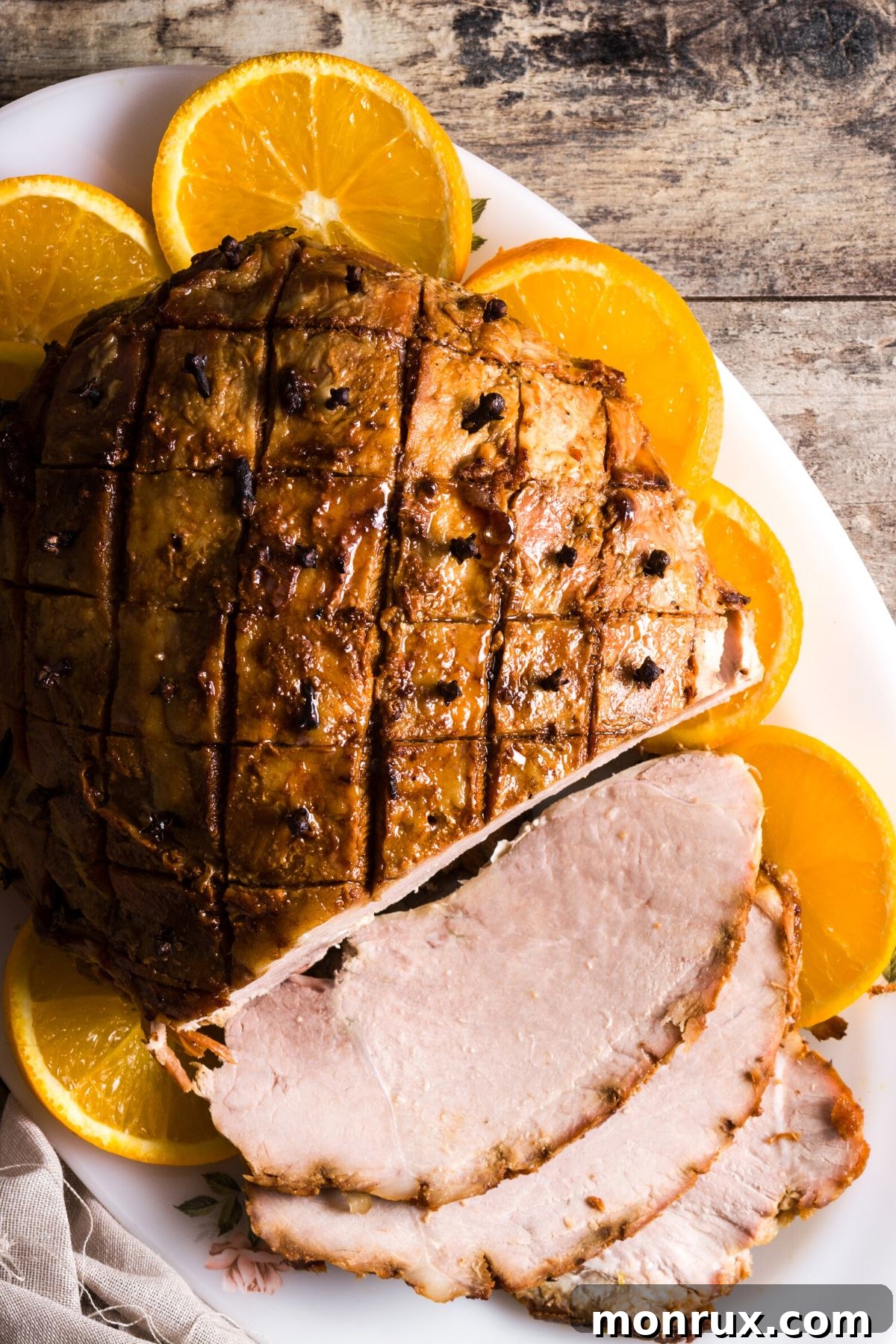 Honey baked ham and orange slices on an oval platter.