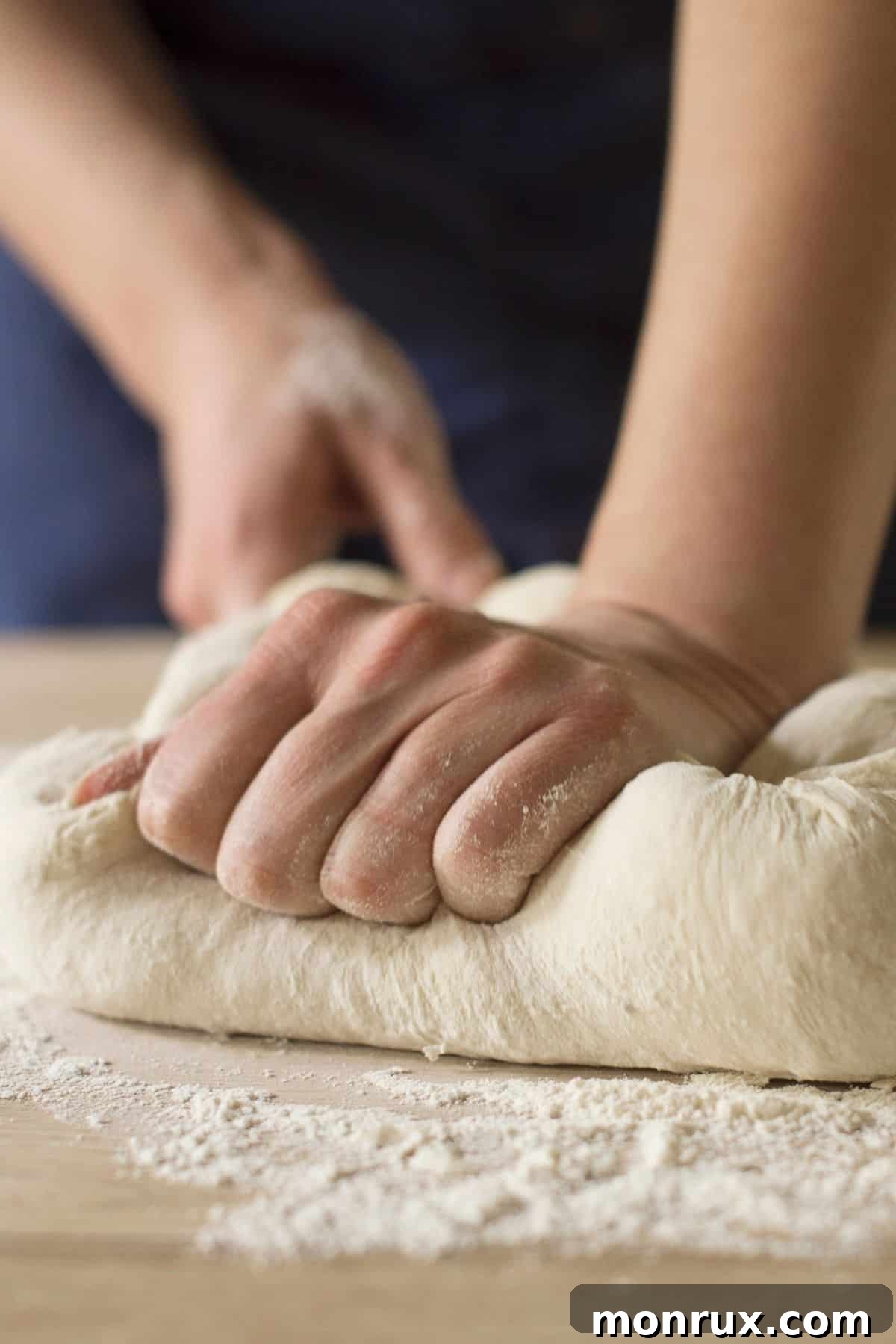 Someone gently kneading a soft ball of gluten-free dough on a lightly floured wooden surface.