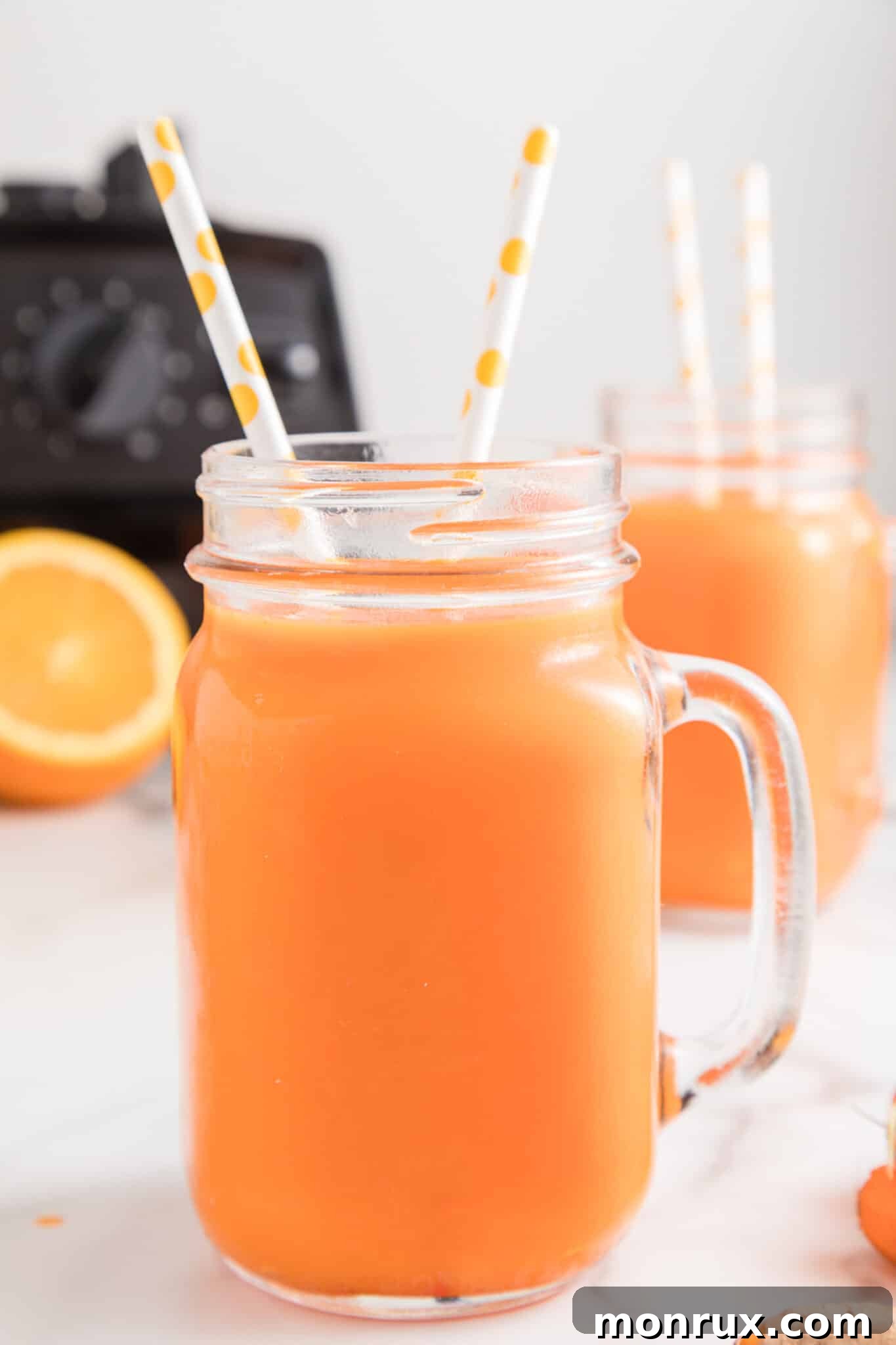 Vitamix carrot juice in a handled mason jar with two paper straws, garnished with an orange slice.