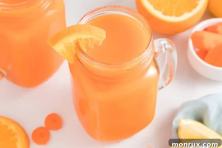 Carrot orange juice in a handled mason jar with an orange slice on the rim, ready to drink.