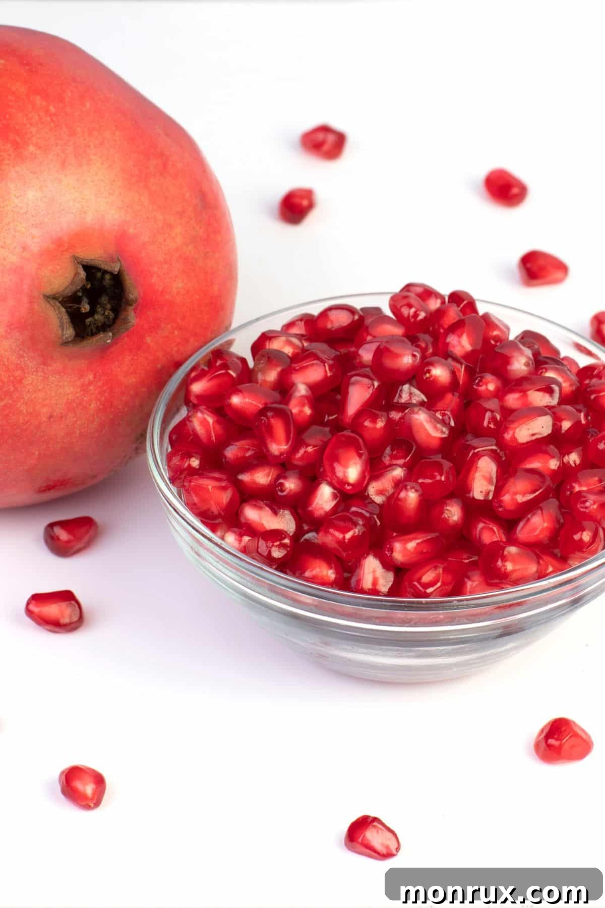 A whole pomegranate next to a small glass bowl of bright red seeds.