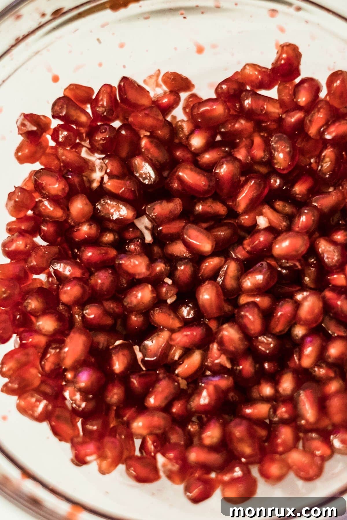 A glass mixing bowl filled with vibrant red pomegranate arils.