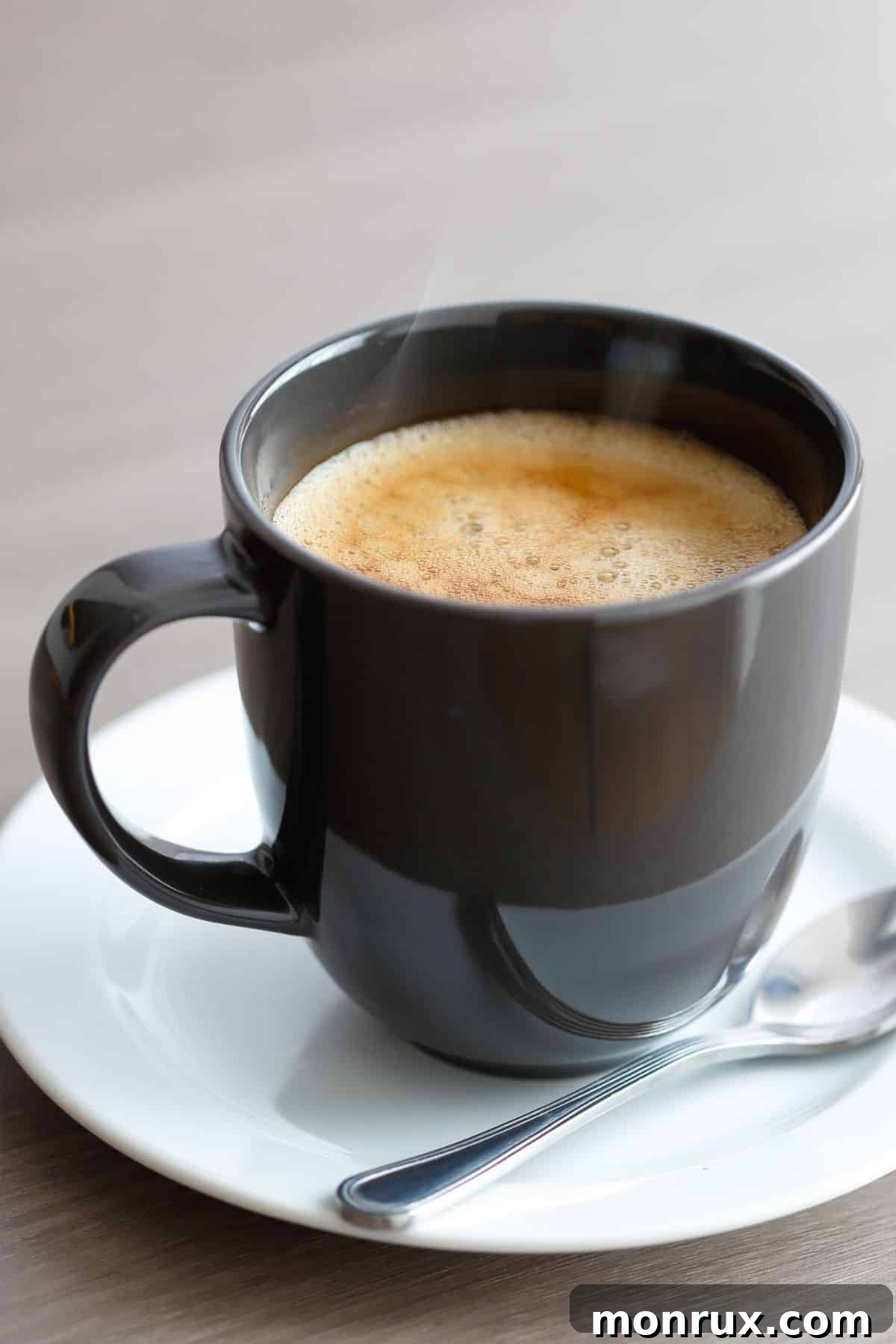 Frothy maca coffee in a black mug on a white saucer, showcasing its rich, creamy texture.