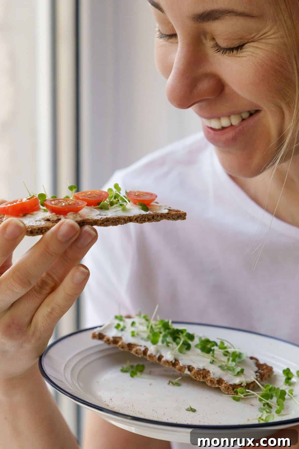 A woman smiling while eating a fresh salad garnished with broccoli microgreens.