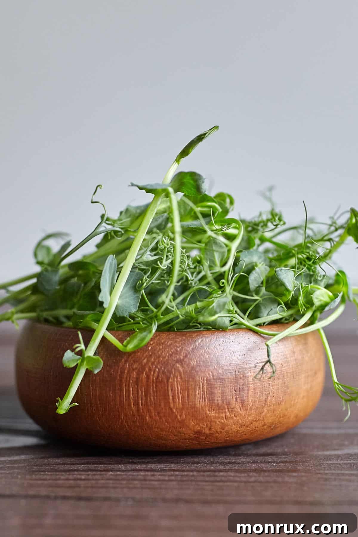 A close-up of a bowl of fresh, green pea microgreens on a wooden table.