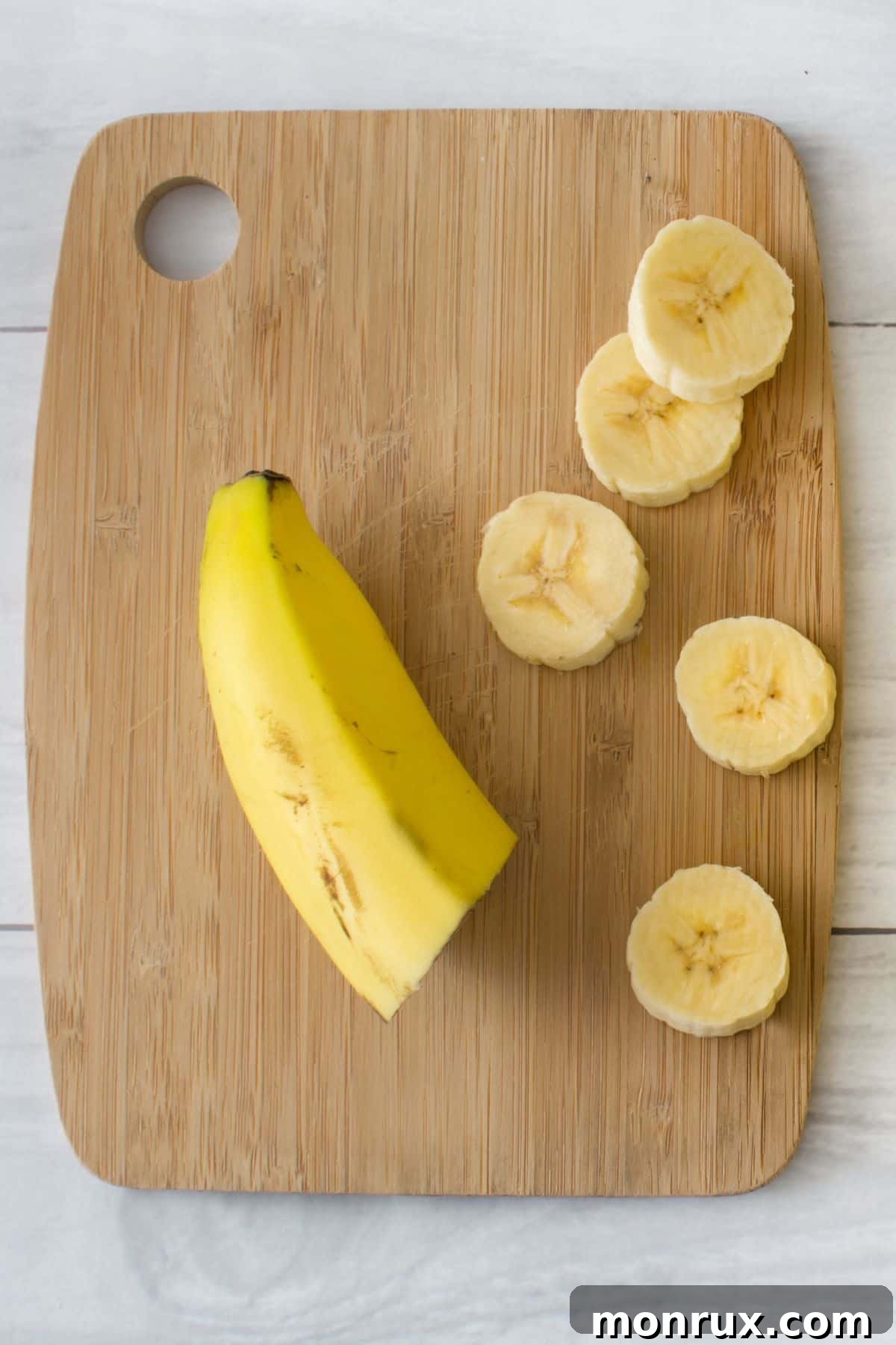 A banana half and several slices arranged on a rustic wooden cutting board.