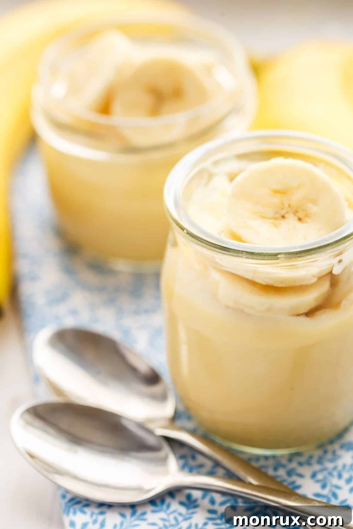 Individual servings of dairy-free banana pudding in small glass jars, resting on a striped linen towel.