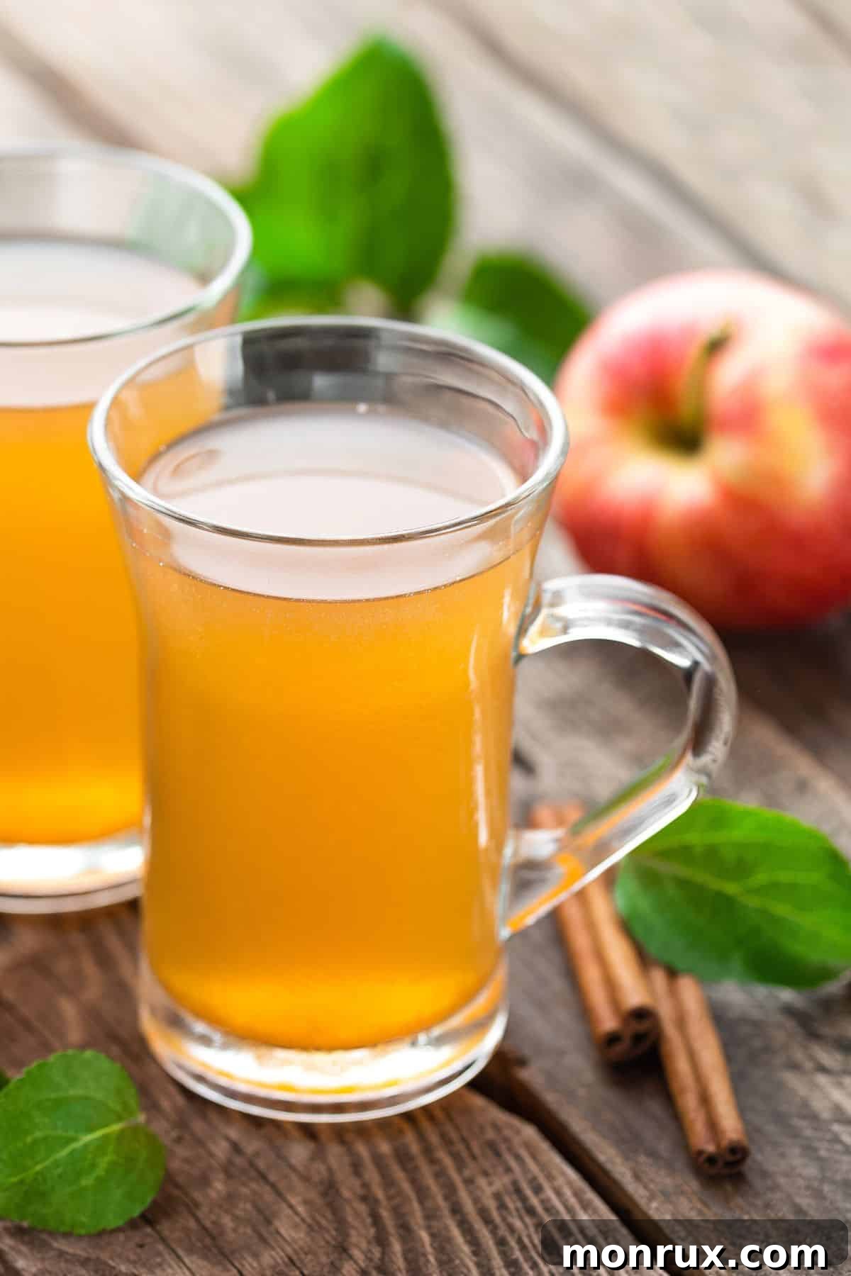 Two mugs of steaming apple cider on a rustic wooden table, garnished with cinnamon sticks and apple slices, evoking warmth and comfort.