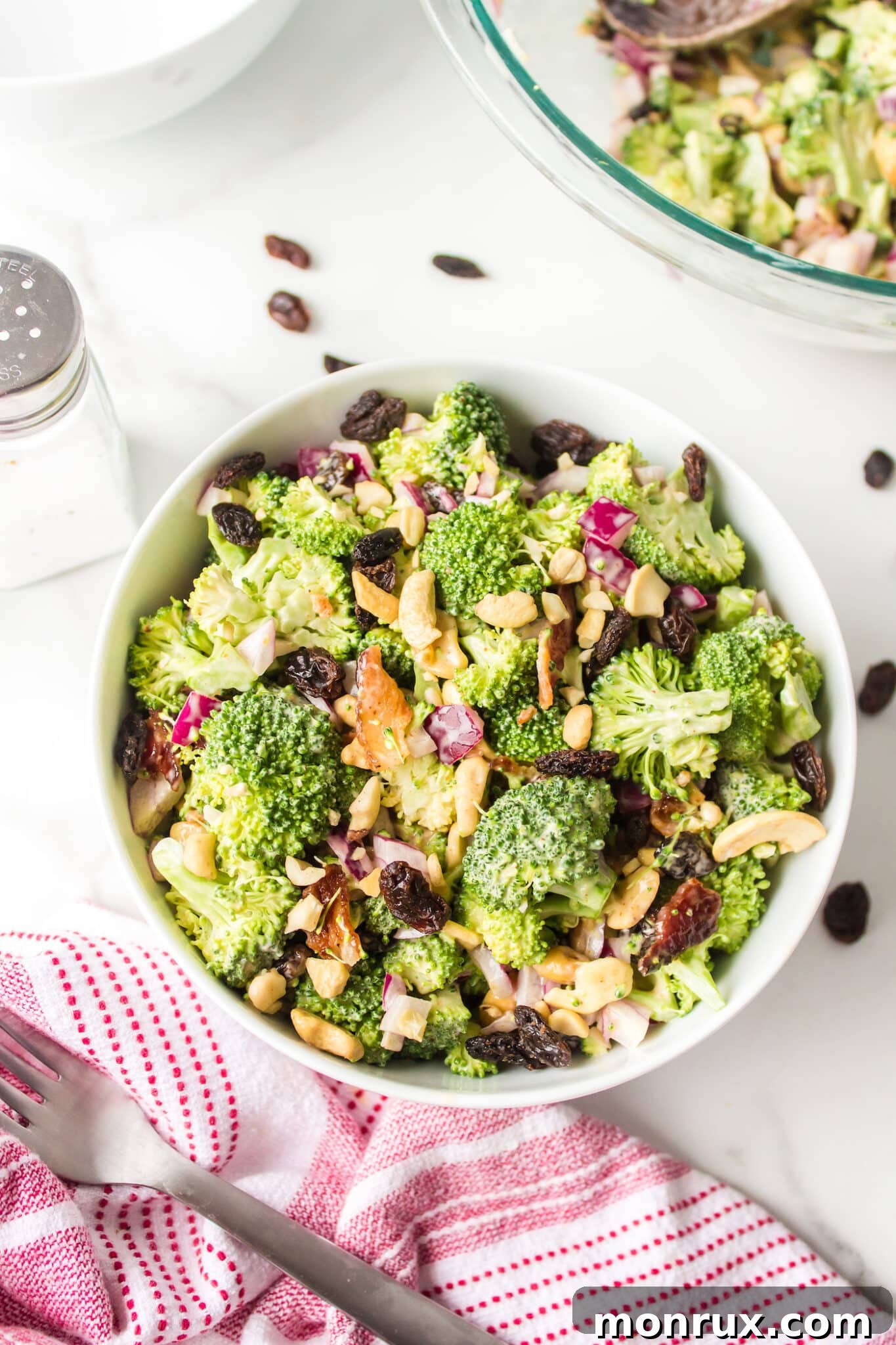 A crisp and colorful Whole Foods style broccoli crunch salad with bacon, raisins, and cashews, served in a pristine white bowl on a light background.