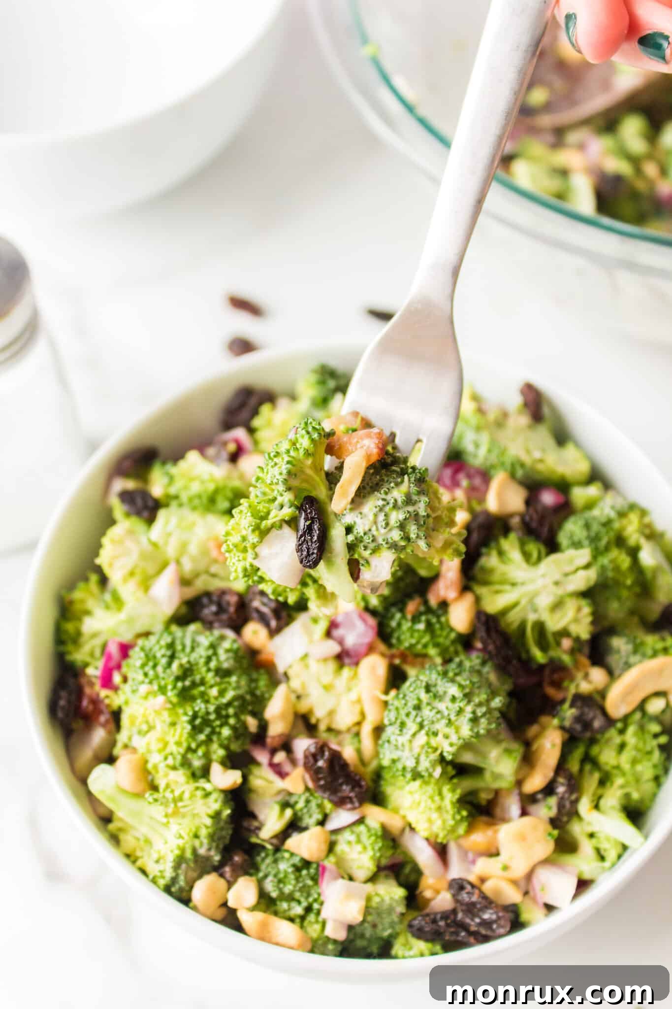 A vibrant and healthy Whole Foods style broccoli crunch salad with visible raisins and cashews, served elegantly in a white ceramic bowl, highlighting its fresh appeal and hearty ingredients.