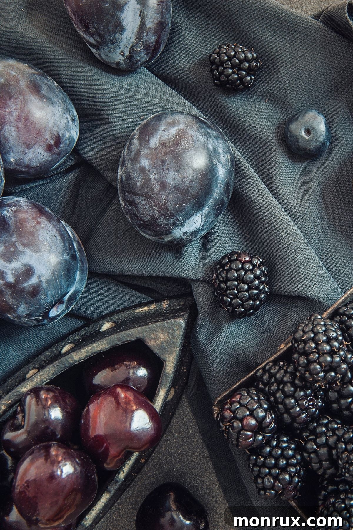 An artfully arranged selection of blue fruits, including blueberries, blackberries, and elderberries, on a navy tablecloth, highlighting their rich colors.
