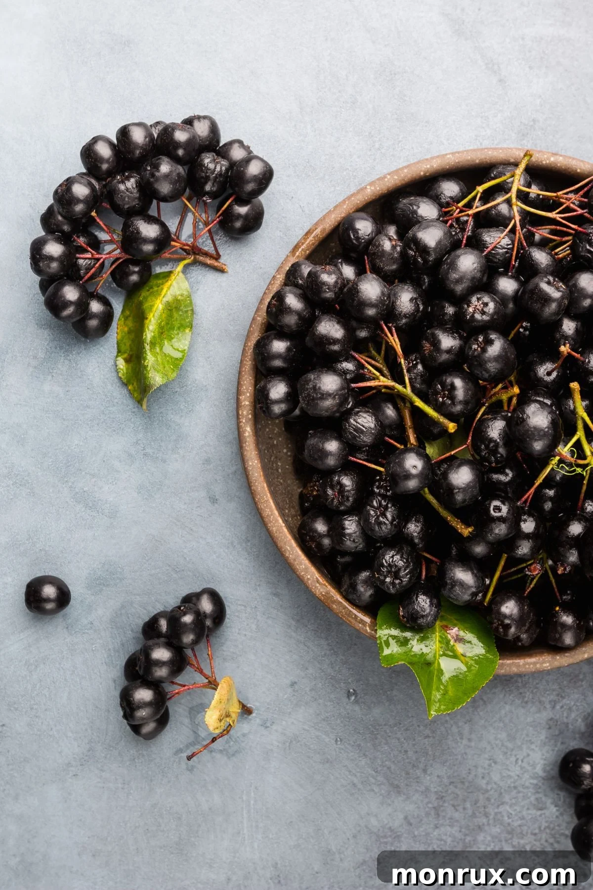 A rustic wooden bowl brimming with chokeberries, showing their deep purple-black color and slightly wrinkled skin.