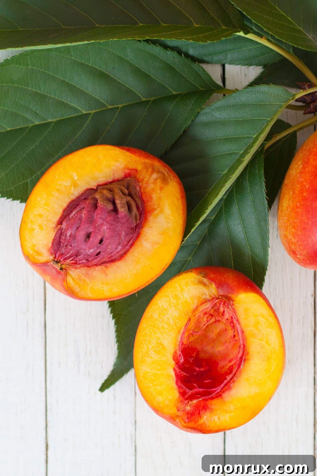 A perfectly sliced nectarine, revealing its juicy, orange-yellow flesh and smooth pit, elegantly arranged on a bed of fresh green leaves.