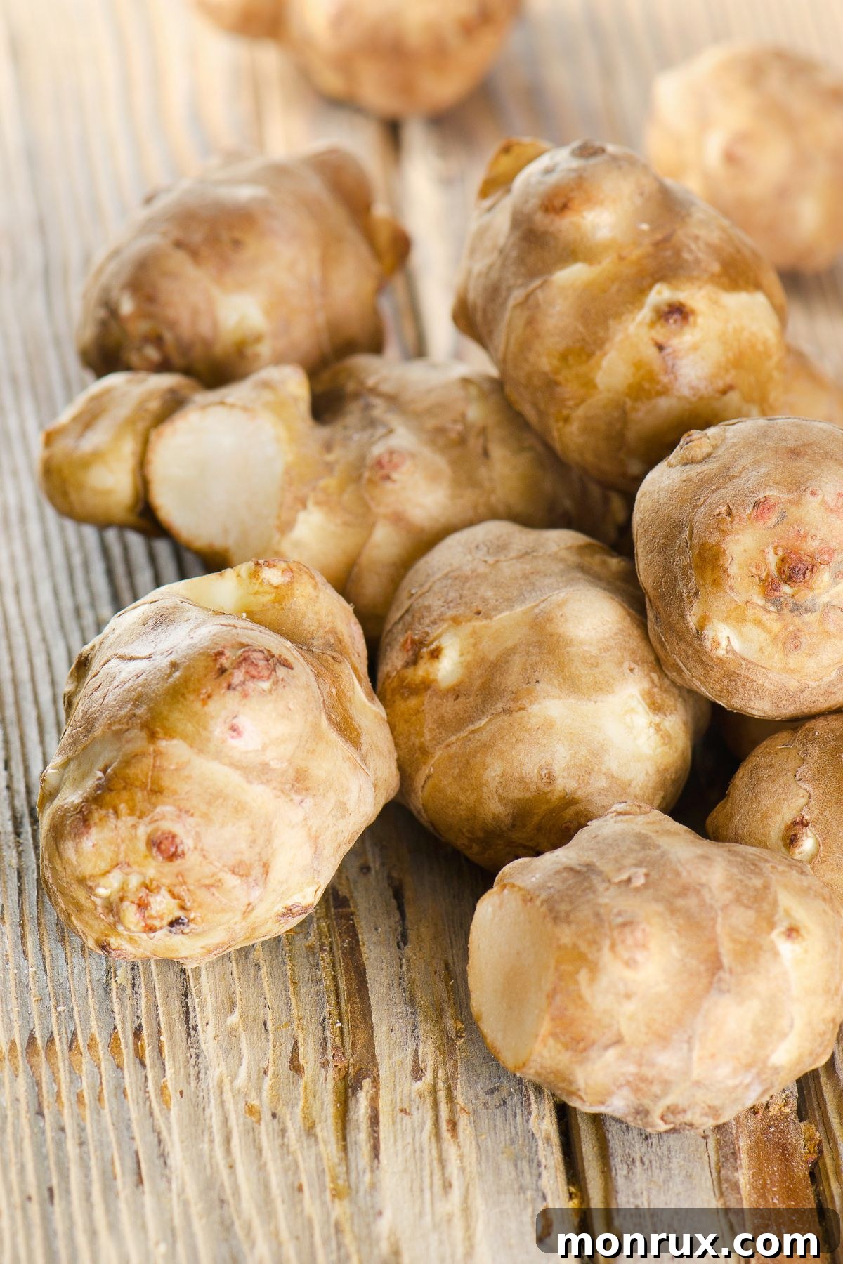 Rustic wooden table displaying a pile of Jerusalem artichokes, showing their irregular, knobby forms.