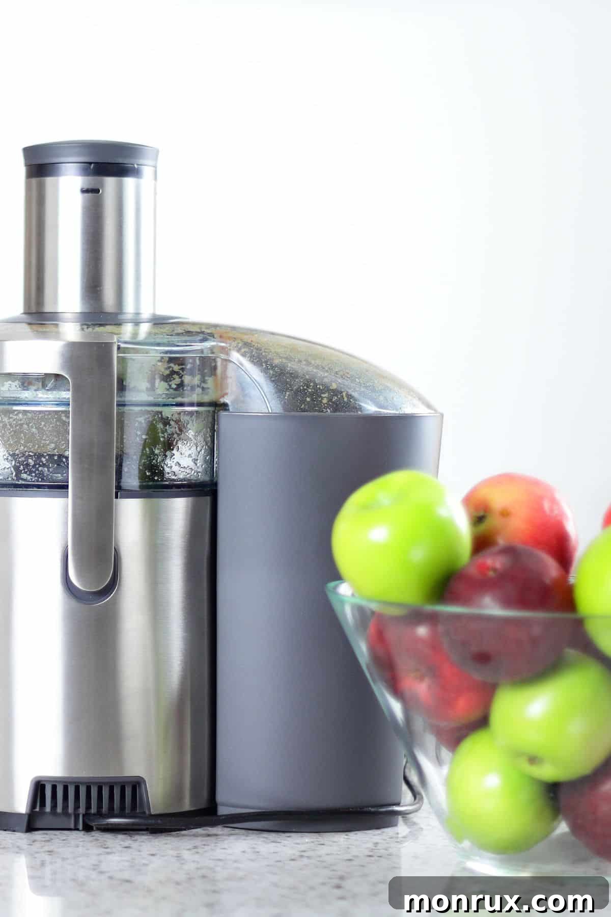 A juicer next to a bowl of red and green apples, ready for juicing.