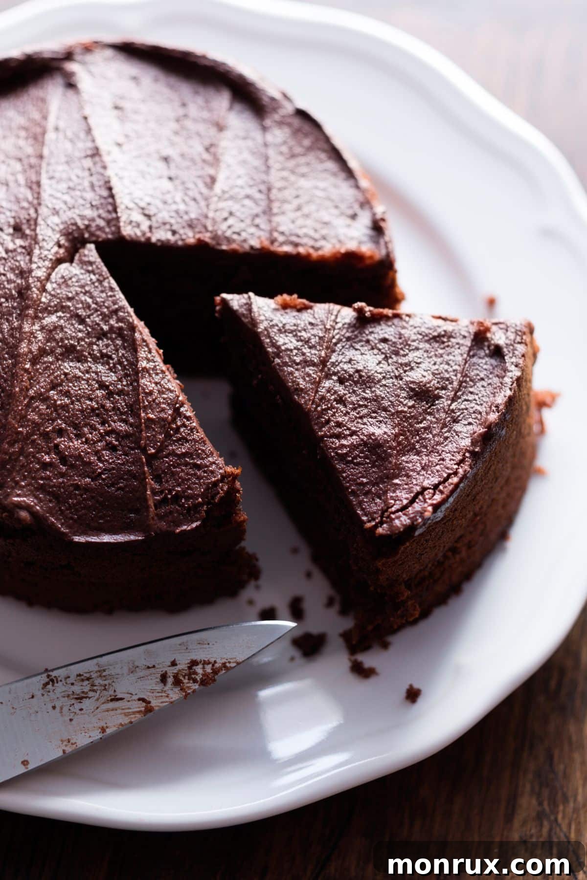 A beautifully decorated round dairy-free chocolate cake on a white plate, with a perfect slice already cut and revealing its moist layers.