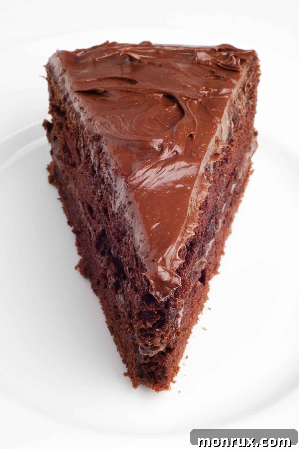 A delectable triangle slice of dairy-free chocolate layer cake, generously frosted and ready to be enjoyed, showing its moist interior.