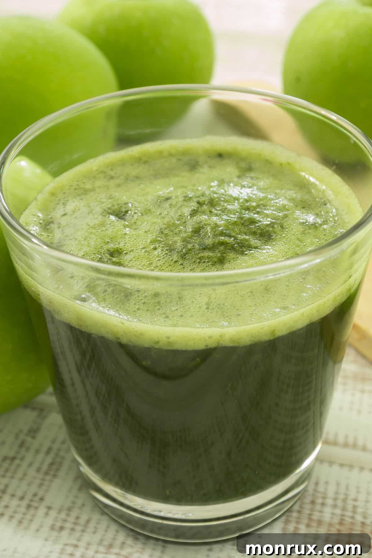A short glass of vibrant green apple juice on a wooden table, accompanied by crisp green apples, suggesting freshness and natural goodness.
