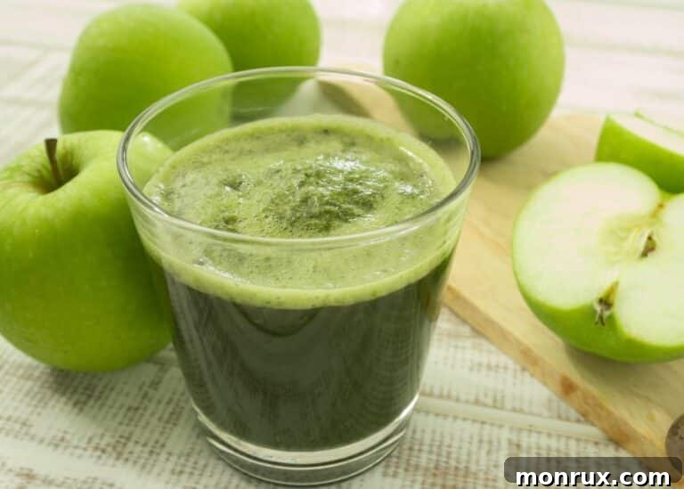 A squat glass of green apple juice on the table with Granny Smith apples, ready to be enjoyed.