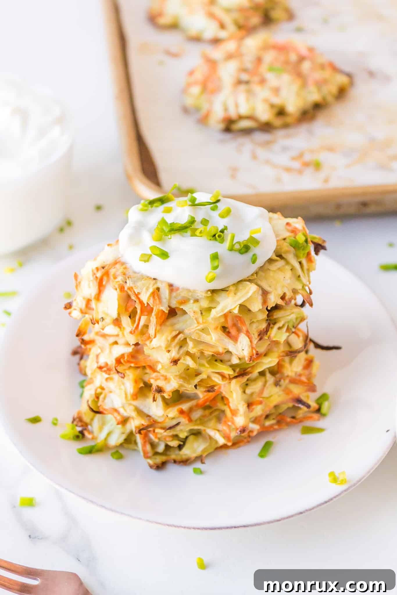 Golden brown cabbage fritters stacked on a white plate, elegantly topped with a dollop of sour cream and fresh chives, ready to be served.