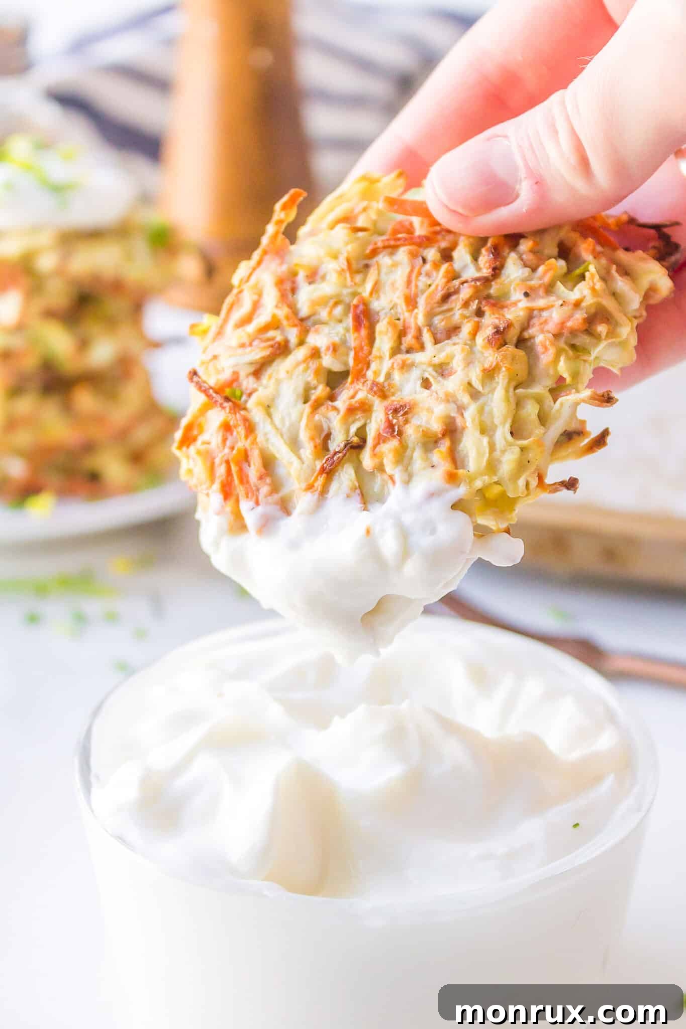 A close-up shot of a hand dipping a warm, baked cabbage fritter into a small bowl of creamy sour cream, highlighting the delicious texture.