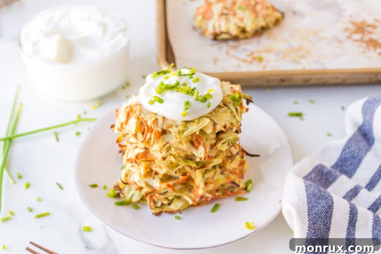 Cabbage fritters stacked on a white plate, topped with sour cream and fresh chives.