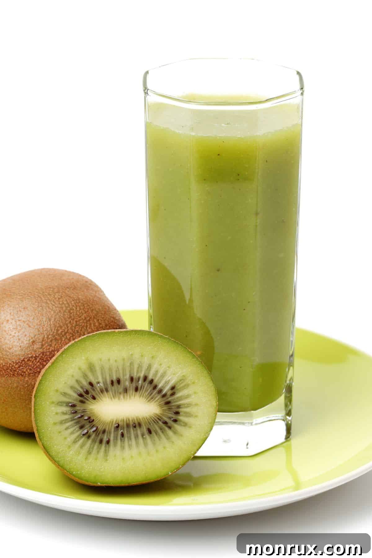 A tall glass of kiwi juice next to two fresh kiwis, one sliced.