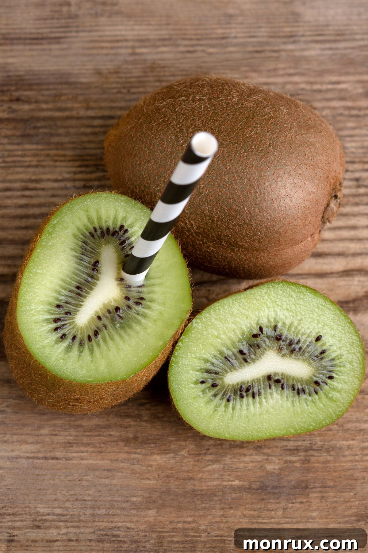 A kiwi cut in half with a straw stuck into it, ready to drink.