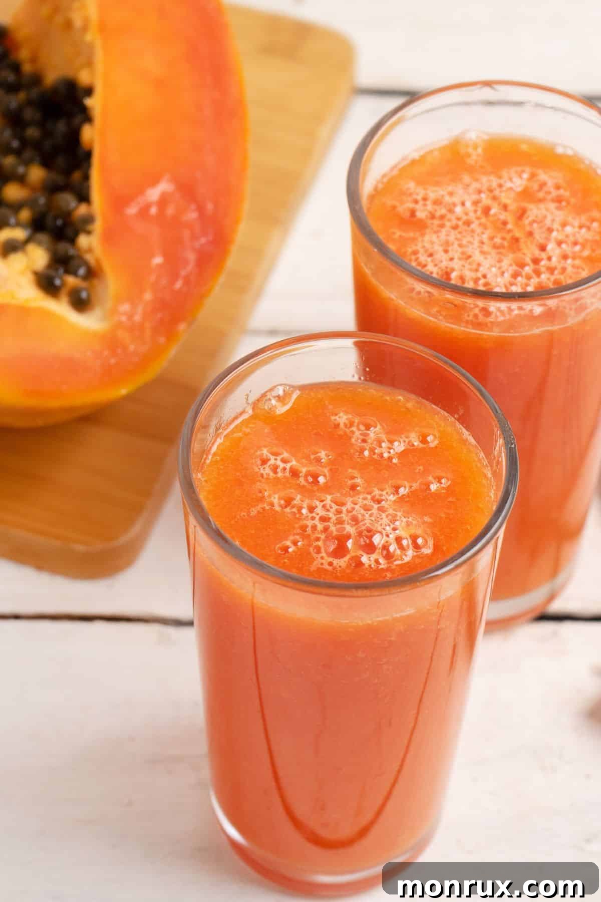 Two glasses of vibrant papaya juice elegantly placed beside a fresh, ripe papaya, evoking a tropical island feel.
