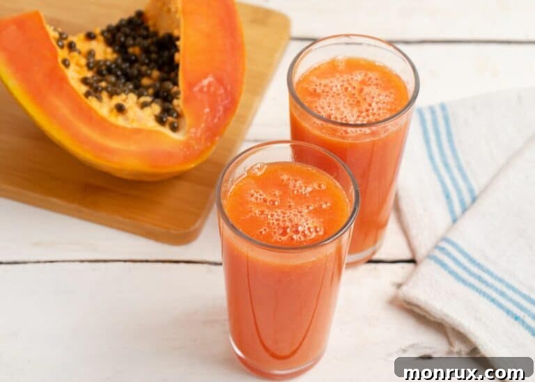 Two glasses of papaya juice next to a fresh papaya, garnished with mint.