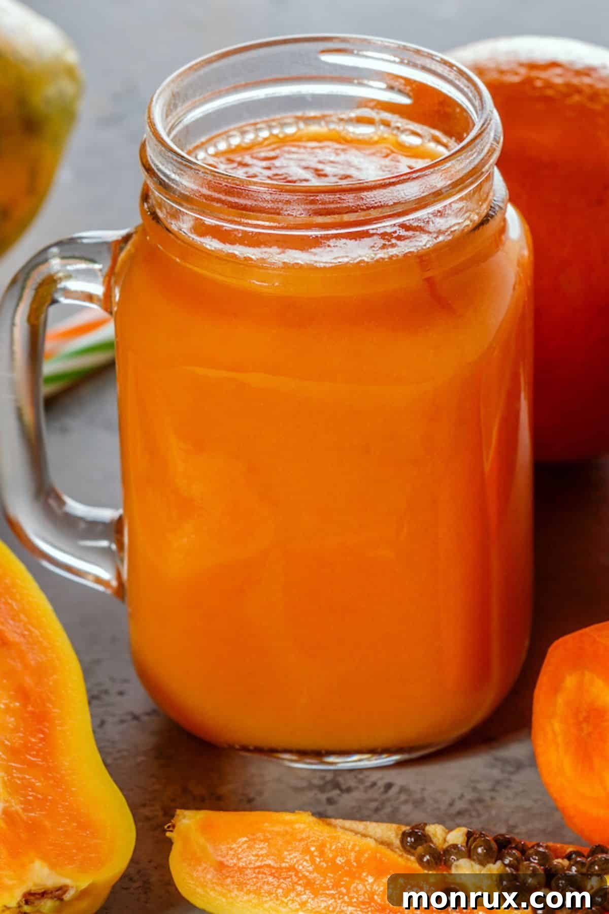 A large, clear handled mason jar filled to the brim with freshly prepared, golden-orange papaya juice, ready for serving.