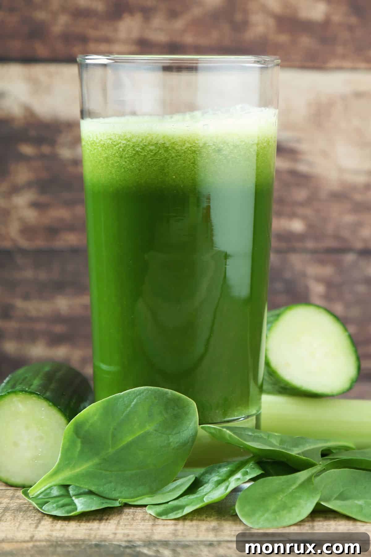 A tall glass of fresh spinach juice, garnished with a spinach leaf, sits on a rustic wooden table.