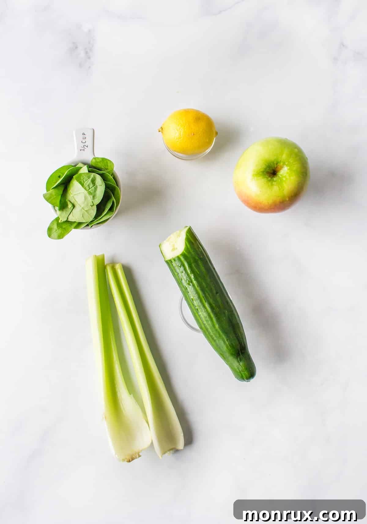 Fresh, vibrant ingredients for making spinach juice arranged on a wooden cutting board: baby spinach, celery, cucumber, green apple, and lemon.