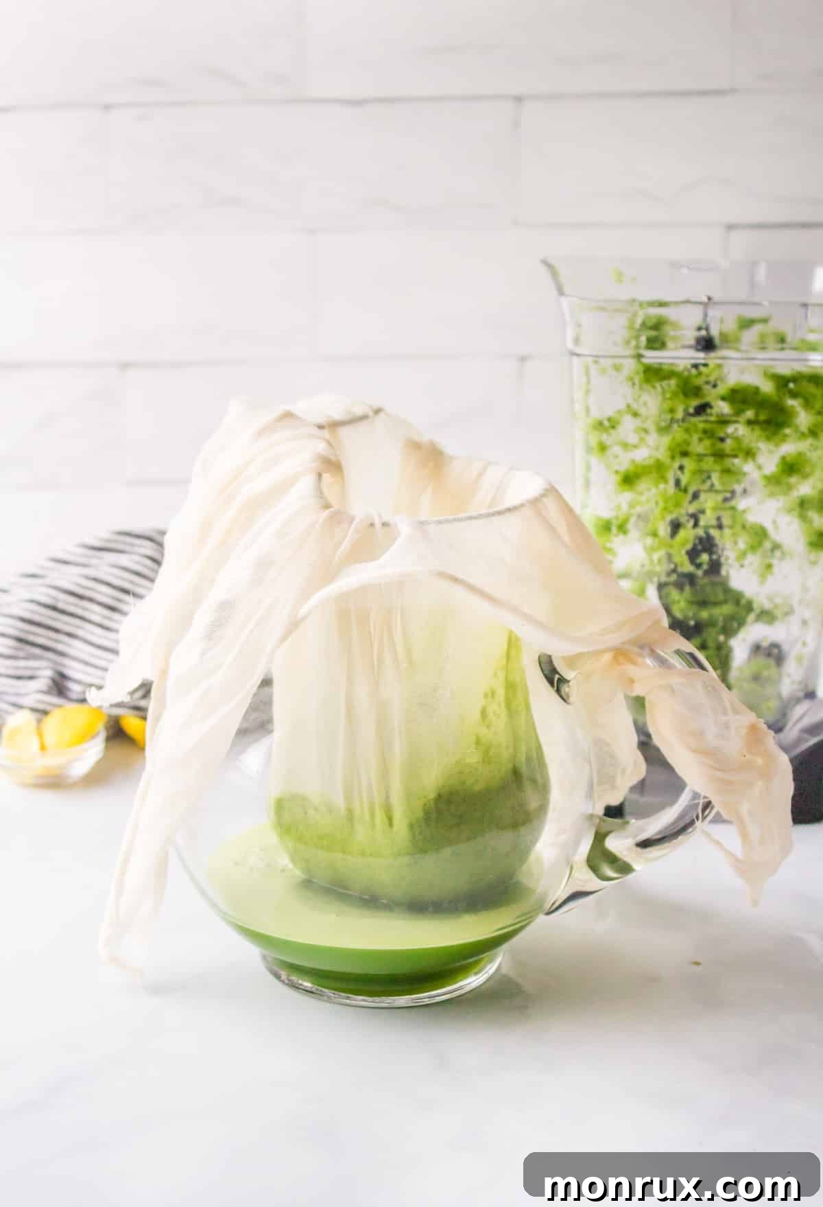 Straining blended green juice through a nut milk bag into a glass pitcher, separating pulp from liquid.