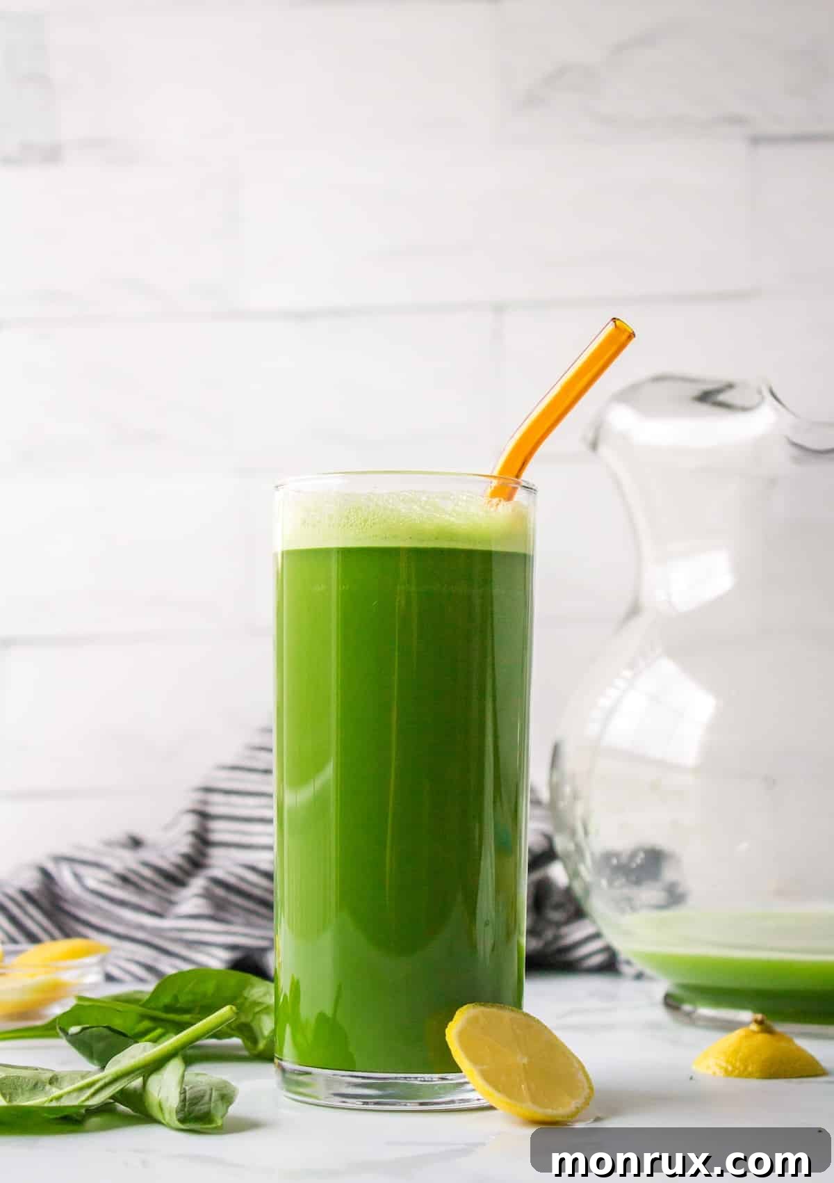 A glass of vibrant green spinach juice served with a straw and a slice of lemon, ready to drink.