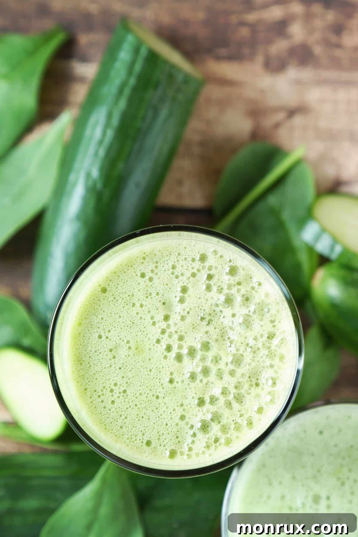Top-down view of a frothy glass of vibrant green spinach juice on a wooden surface, with a faint shadow.