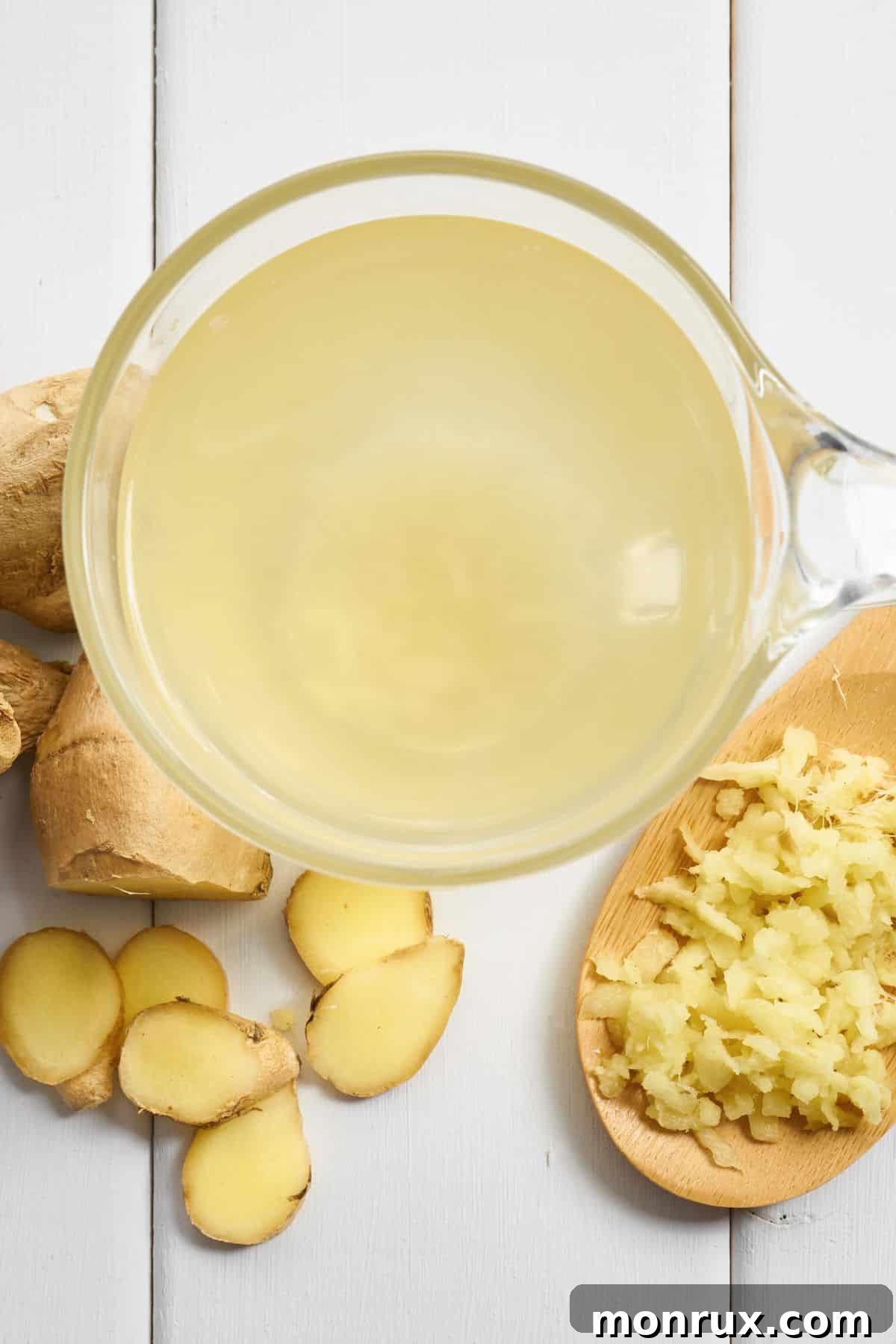 A small glass of ginger juice with fresh ginger on a white wooden surface.