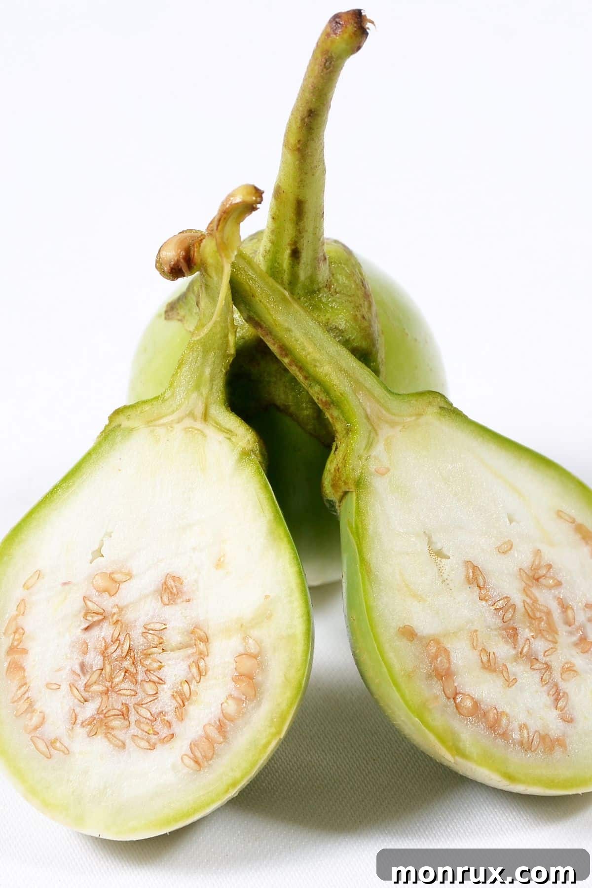 A sliced open Thai eggplant rests against a whole Thai eggplant, revealing its pale interior.