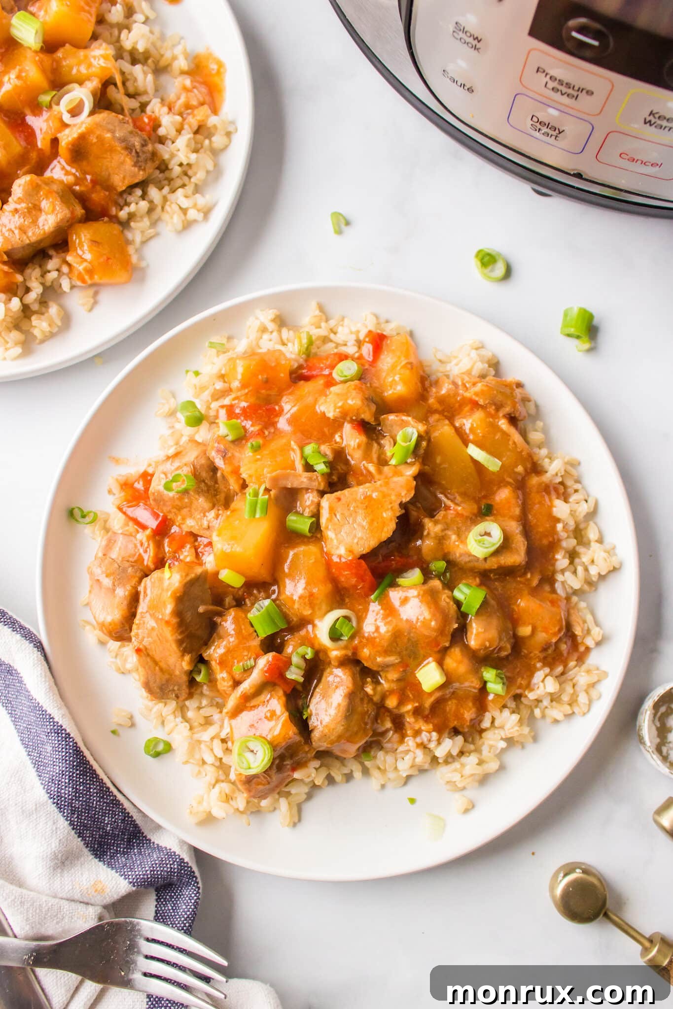 A white dinner plate of brown rice topped with sweet and sour pork.
