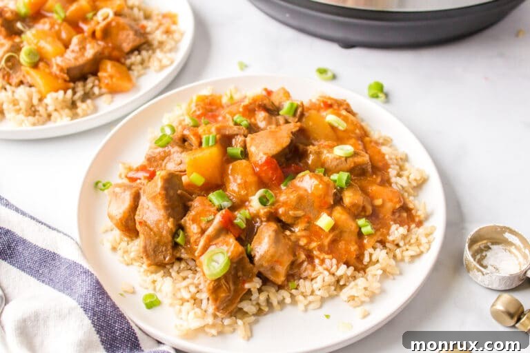 A white dinner plate of brown rice topped with sweet and sour pork.